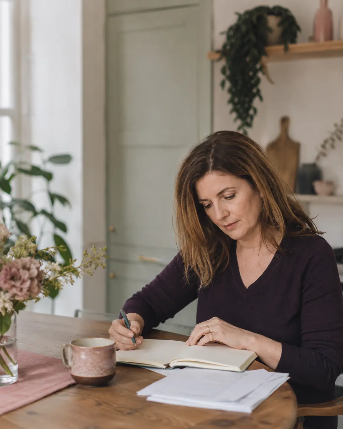 A woman writing in a notebook at her kitchen table